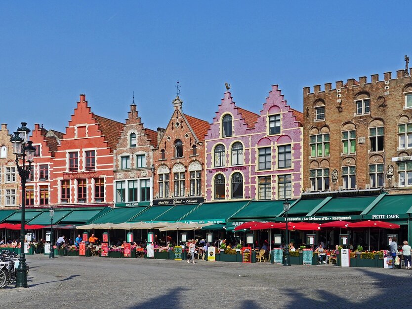 Großer Marktplatz mit vielen Ständen und bunten Häusern im Hintergrund in Brügge, Belgien