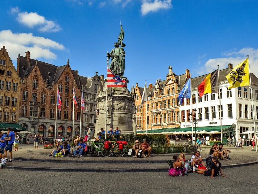 Großer Marktplatz im Sommer mit vielen Menschen und bunten Häusern in Brügge, Belgien