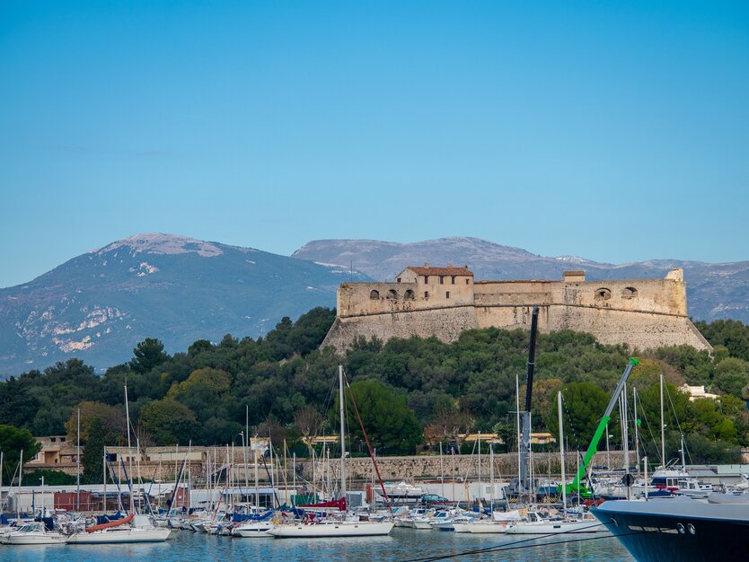 Städtereise Nizza, Frankreich, Ausflug nach Antibes, Blick auf den Hafen mit Booten und die dahinterliegenden Berge und ein altes Haus auf einem bewachsenen Hügel, Meer, Panorama, gutes Wetter