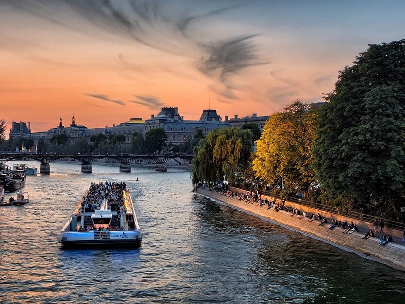 Städtereise Paris, Frankreich, Bootsfahrt, Blick auf ein Touristenboot an der Seine bei Dämmerung, Brücken, Gebäude und Ufer