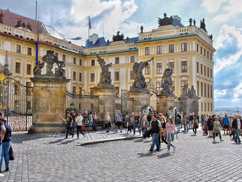 Städtereise Prag, Tschechien, Ausflug Prager Burg, Menschen auf dem Vorplatz vor den Eingangstoren der Prager Burg, gelbes Gebäude, Aussicht, blauer Himmel