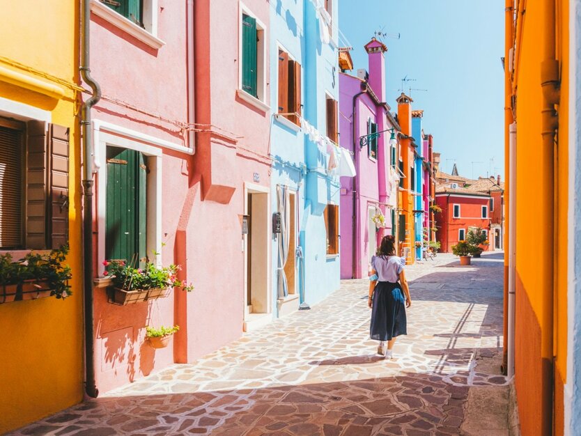 Städtereise Venedig, Italien, Rundum sorglos Paket, bunte Häuser in einer Gasse mit einer Frau, blauer Himmel